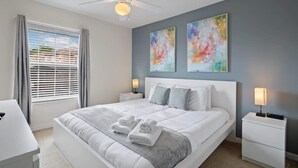 Een slaapkamer met een bed, twee nachtkastjes, een plafondventilator en twee abstracte schilderijen aan de muur.