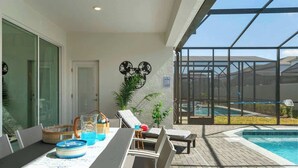 Een terras met een eettafel, lounge stoelen, een zwembad en een glazen ruimte versierd met een Mickey Mouse decoratie.