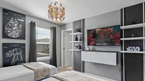 Een slaapkamer met twee bedden, Star Wars decoratie, een groot poster en een moderne kroonluchter.