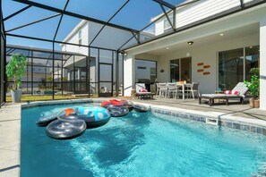 A swimming pool with inflatable rings, a covered patio with a table and chairs, and a view of a house in the background. - 5BD Windsor Island Star Wars Game Room (WI 3408) (Davenport)
