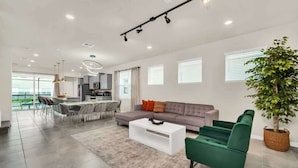 Una sala moderna con sofá, mesa de centro y sillas, un comedor con mesa y sillas, y una cocina al fondo.