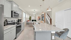 Una cocina moderna con una isla central, electrodomésticos de acero inoxidable e iluminación colgante.