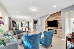 A modern living room with a grey sofa, blue chairs, a flat-screen TV, and a fireplace. - 5BD Windsor Westside Near Disney (WW 9004) (Kissimmee)