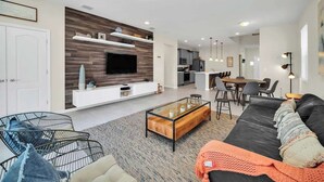A modern living room with a sofa, coffee table, and TV. There is a dining area with chairs and a table. - 7BD Windsor Westside Near Parks (WW 2485) (Four Corners)