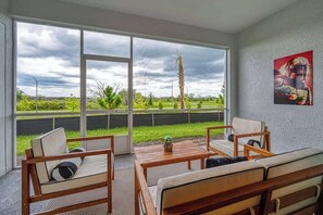 A room with a large window, a wooden table, two chairs, a sofa, and a wall-mounted artwork.