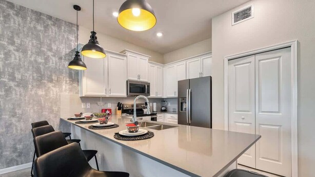 A modern kitchen with a central island, white cabinets, stainless steel appliances, and black bar stools.