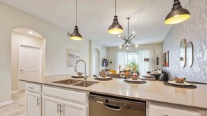 A kitchen with a central island, white cabinetry, a dishwasher, pendant lighting, and a dining area with chairs and a table.