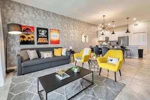 Uma sala de estar moderna com um sofá, mesa de centro e cadeiras amarelas. Há decorações nas paredes, uma área de refeições e uma cozinha ao fundo.