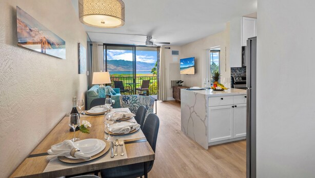 Una cocina moderna con armarios blancos, un refrigerador empotrado y un comedor con una mesa de madera preparada para cuatro comensales.