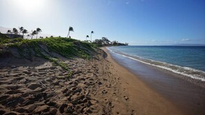 A beach with footprints, palm trees, and a clear sky. - Oceanfront Maui Condo Renovated 2BR/2BA, Pool & Sunsets — Featured on Staycation (Kihei)