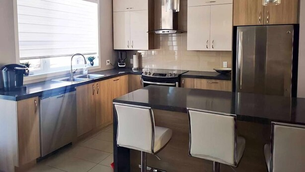 Een moderne keuken met roestvrijstalen apparatuur, houten keukenkastjes en een centraal kookeiland met barkrukken.