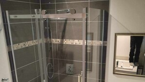 Een moderne badkamer met een douche met glazen wand, een toilet en een prullenbak.
