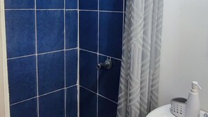 A bathroom with blue tiled walls, a shower with a white curtain, and a white sink with a bottle of shampoo. - Comfy Stay for 2 @CasaSanAlfonso Room #21 (San Alfonso)