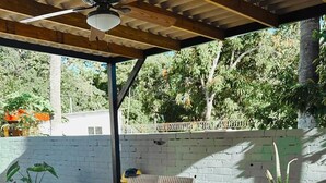Une terrasse couverte avec une table en bois, des meubles en osier et un ordinateur portable.
