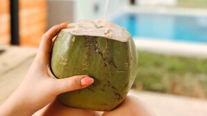 Une personne tenant une noix de coco avec une paille, avec une piscine et de la verdure en arrière-plan.