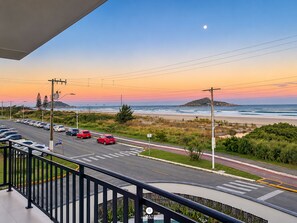A coastal road with cars, a pedestrian crossing, and a view of the ocean at sunset.