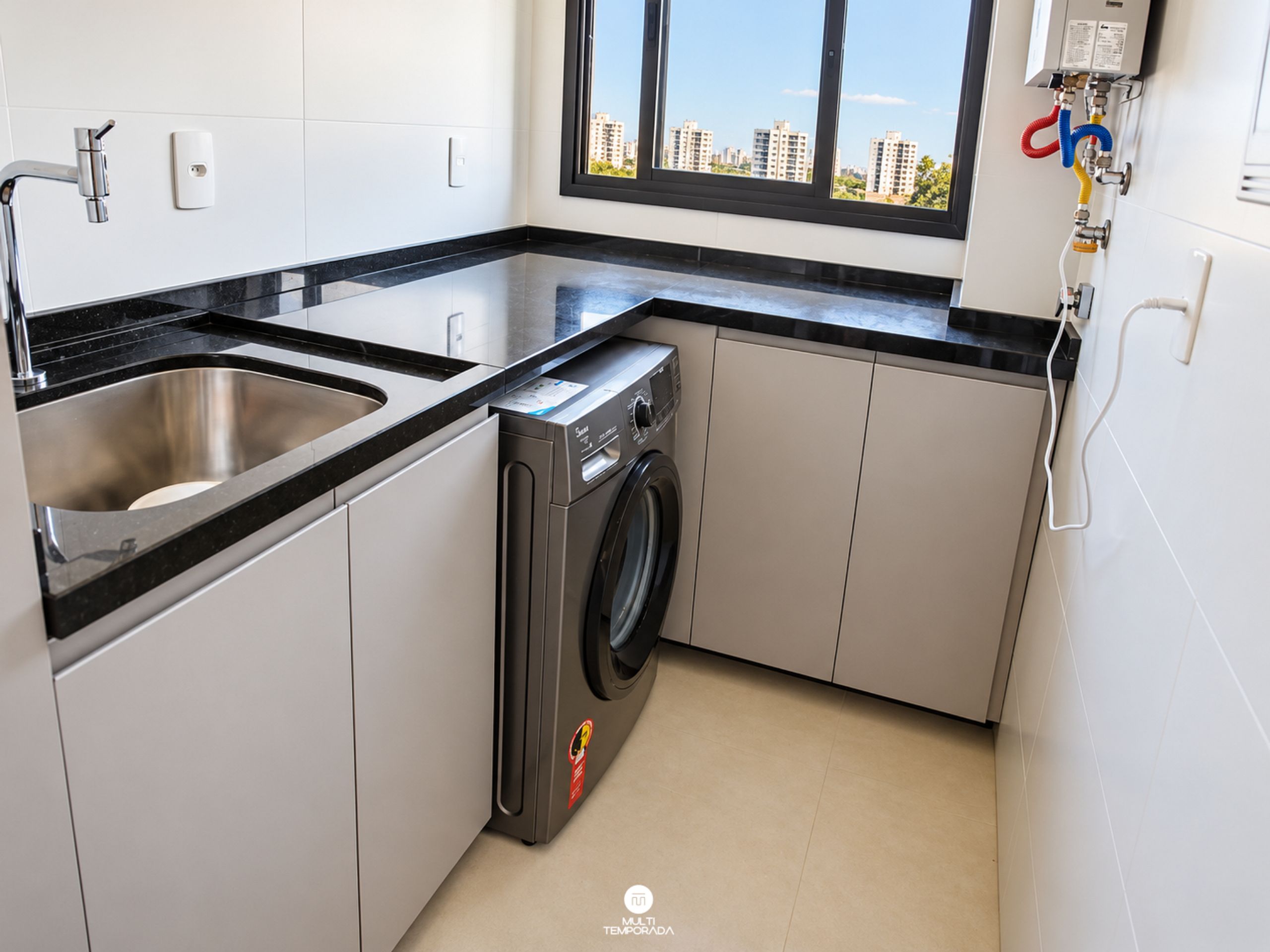 Una cocina compacta con pileta de acero inoxidable, lavadora integrada y ventana con vista a la ciudad.