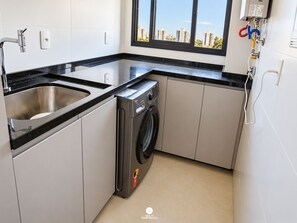 Een kleine keuken met een RVS spoelbak, een ingebouwde wasmachine en een raam met uitzicht op de stad.