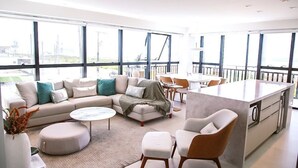 A modern living area with a sofa, ottoman, coffee table, and a kitchen island. - Apto Pe na Areia - Frente Mar - Imbituba (Imbituba)