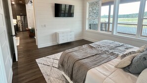 A bedroom with a large bed, a ceiling fan, a TV mounted on the wall, and a window with a view of the outdoors. - “Stay in this brand new luxurious cabin in Hochatown.  (Broken Bow)