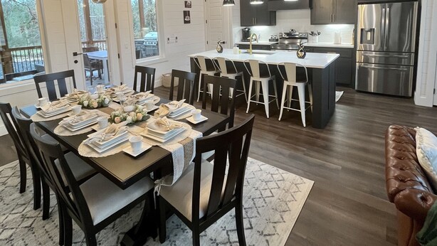 A modern kitchen with dark cabinetry, stainless steel appliances, and a dining area with a set table. - “Stay in this brand new luxurious cabin in Hochatown.  (Broken Bow)