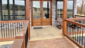 A wooden deck with a stone wall and a wooden door leading to a covered porch. - “Stay in this brand new luxurious cabin in Hochatown.  (Broken Bow)