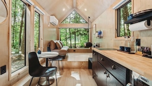 Ein modernes Blockhaus-Interieur mit Essbereich, Küche und großem Fenster mit Blick auf einen Wald.
