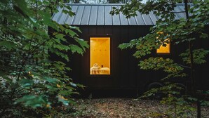 Una cabaña aislada con exterior oscuro, dos ventanas iluminadas y entorno boscoso.