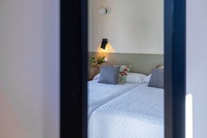 A hotel room with two beds, a nightstand, a lamp, and a wall-mounted light fixture.