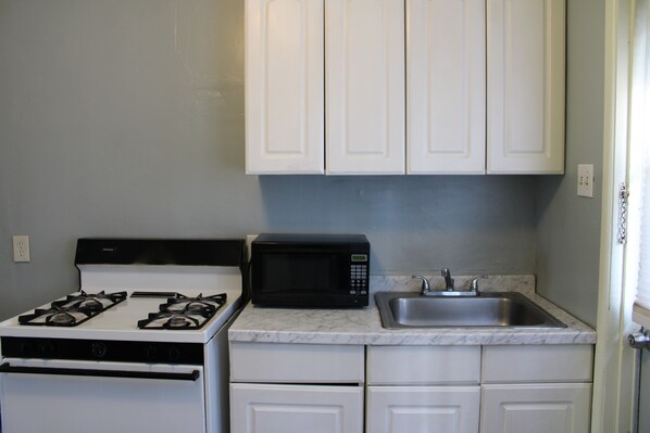 A compact kitchen with white cabinets, a stove, a microwave, and a sink.