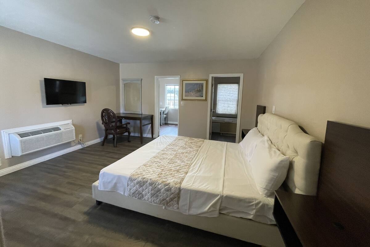 A bedroom with a bed, a desk, a chair, a television, and a window.