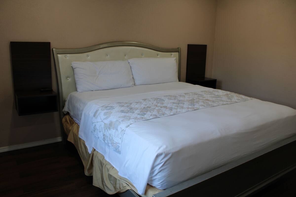 A neatly made bed with a headboard, a bedside table, and a wall-mounted speaker on either side.