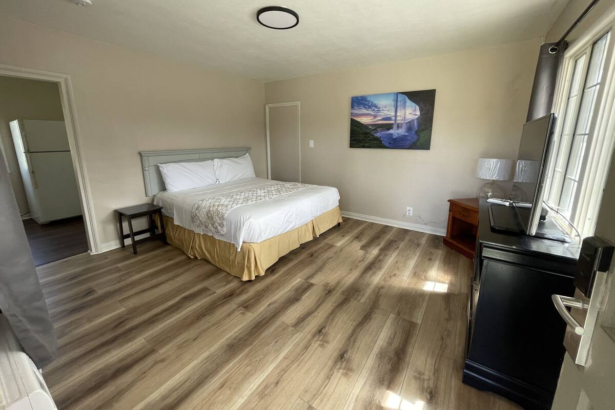 A bedroom with a bed, a dresser, a painting, and a window.