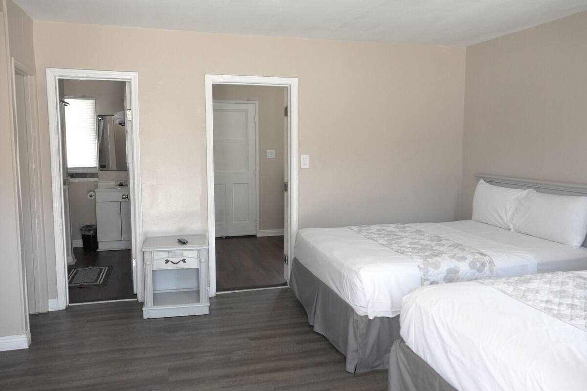 A bedroom with two beds, a small bedside table, and a door leading to a bathroom.