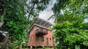 A two-story building with a balcony, surrounded by dense greenery.