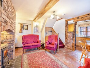 Um quarto aconchegante com lareira, um sofá vermelho estampado, uma poltrona combinando, uma escada e uma mesa de jantar de madeira com cadeiras.
