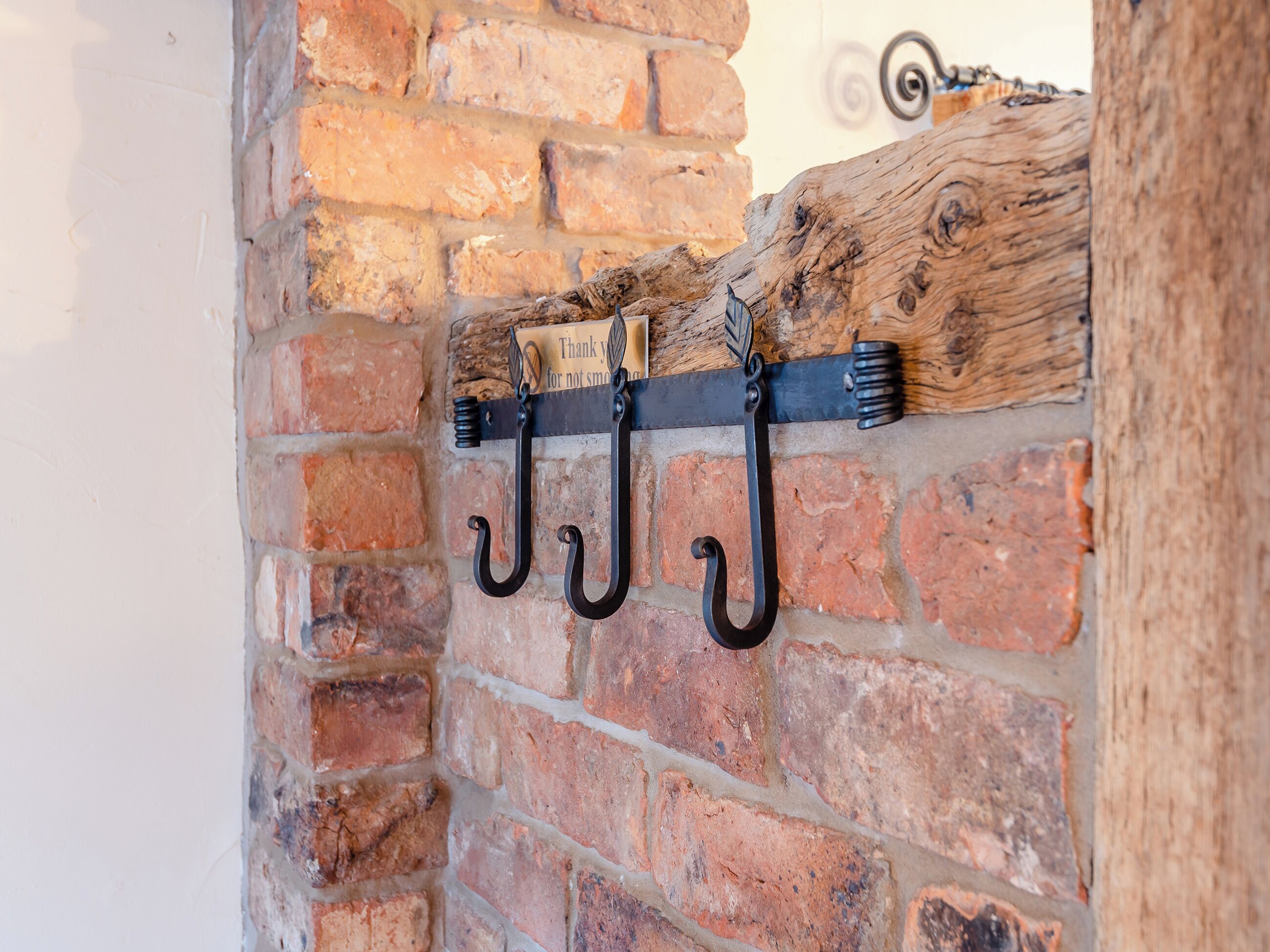 A brick wall with a wooden beam and three black hooks mounted on it.