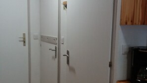 Ein Flur mit zwei weißen Türen, einem Kleiderhaken, einem Holzschrank und einem karierten Stoffbild an der Wand.