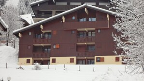 Ein mehrstöckiges Gebäude mit Balkonen, umgeben von schneebedeckten Bäumen und einer verschneiten Fläche.