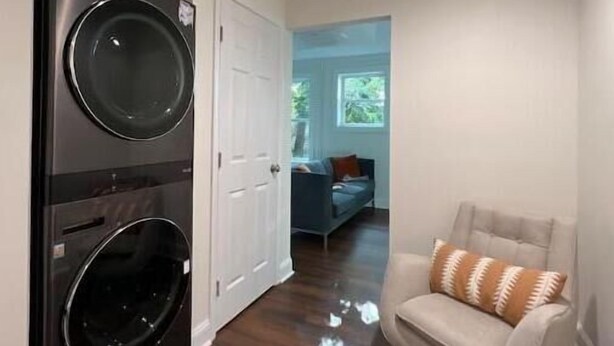 Une buanderie équipée de deux machines à laver et deux sèche-linge superposés, une porte blanche et une chaise avec un coussin à motifs.
