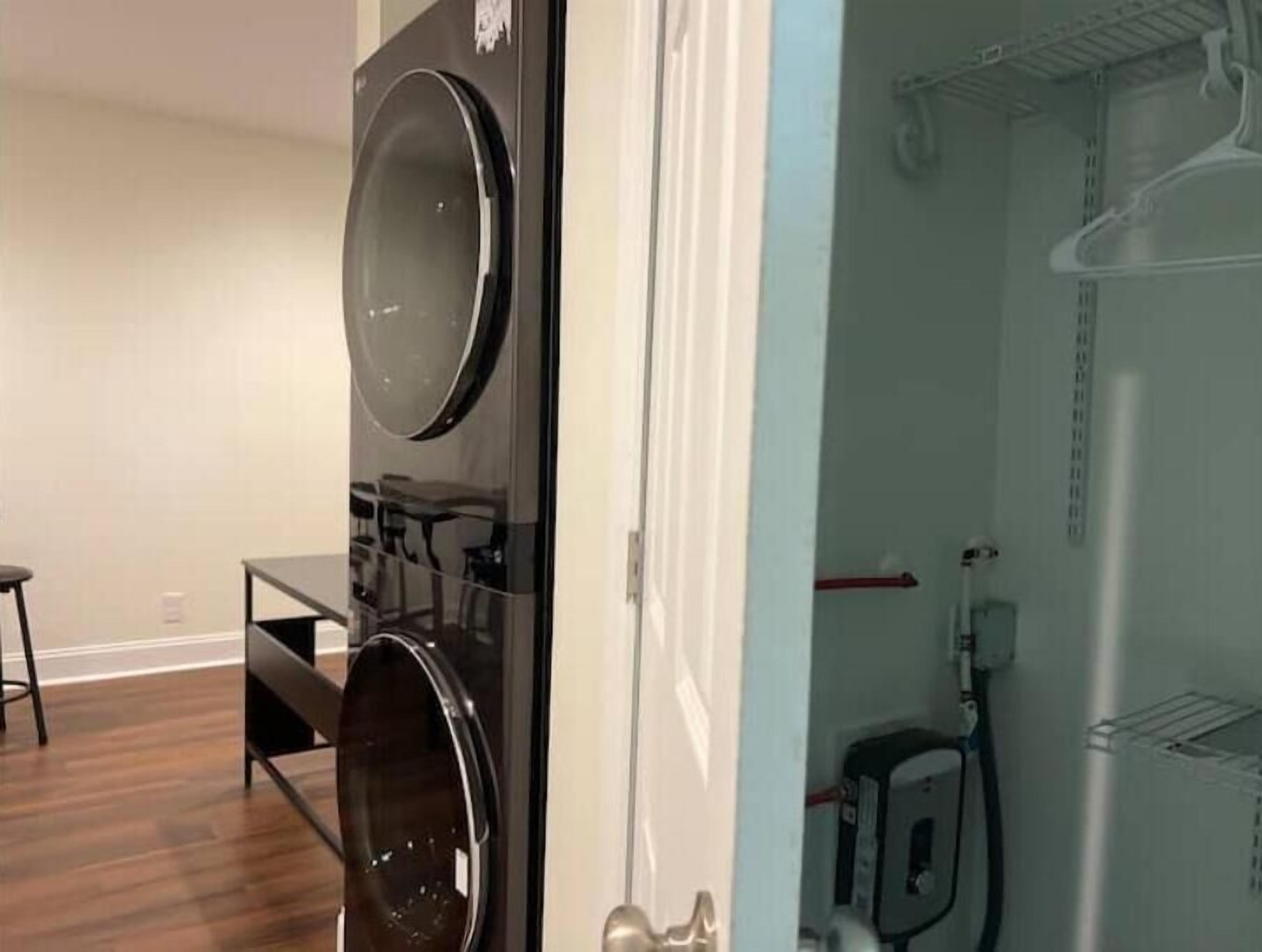 A laundry room with a large, modern washer and dryer, a small table, and a bench.