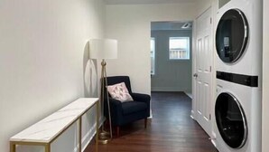 A laundry room with two front-loading washing machines, a bench, and a chair.