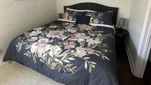 A bedroom with a floral bedspread, a round wall clock, and a painting on the wall.