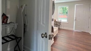 A room with a wooden floor, a white door, and a view of a dining area with a window.