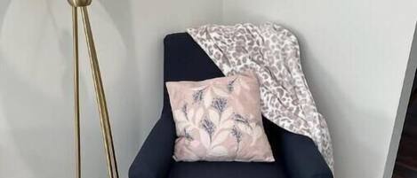 Habitación en esquina con un sillón azul oscuro, una lámpara de pie dorada y una manta de estampado de leopardo.