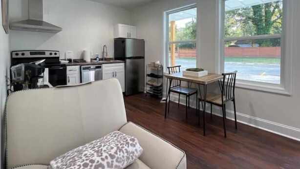 A compact kitchen with modern appliances, a dining area with a wooden table and chairs, and a large window offering a view of the outdoors.