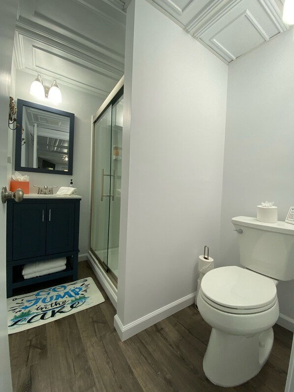 Une salle de bain avec un meuble-lavabo bleu foncé, une douche en verre, des toilettes blanches et un tapis blanc orné de motifs textuels.