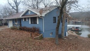 Una casa blu con un molo che si protende su un corpo d'acqua, circondata da alberi e foglie cadute.