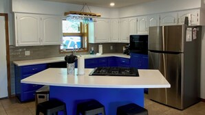 Una cucina moderna con mobili bianchi, un frigorifero in acciaio inox, un'isola azzurra con sgabelli e un lampadario a sospensione.