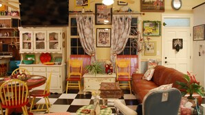 Una sala de estar acogedora con piso a cuadros, un sofá de cuero marrón, una mesa de comedor con sillas, un televisor y varias decoraciones.